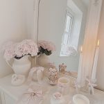 Large white vintage mirror on a shabby chic vanity with pink hydrangeas a bow mug and burning scented candles