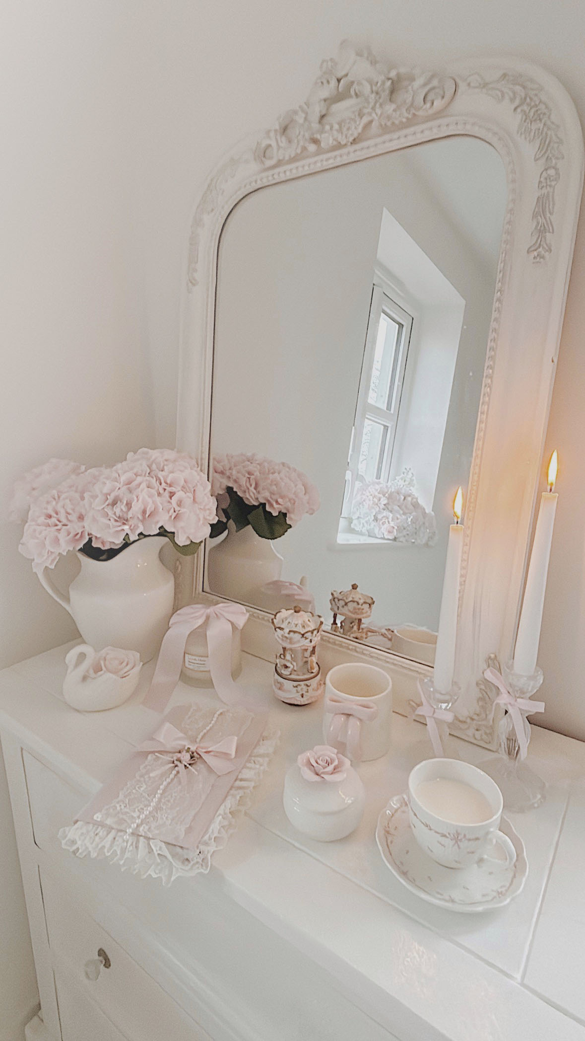 Large white vintage mirror on a shabby chic vanity with pink hydrangeas a bow mug and burning scented candles
