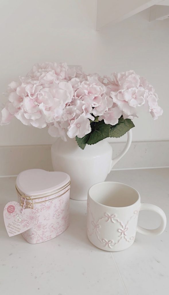Vase with pink hydrangeas and a pink bow mug on a marble kitchen counter