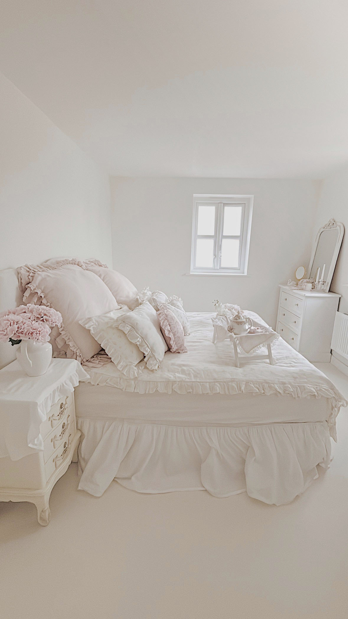 Shabby chic bedroom side view with white ruffled bed skirt and natural window light.